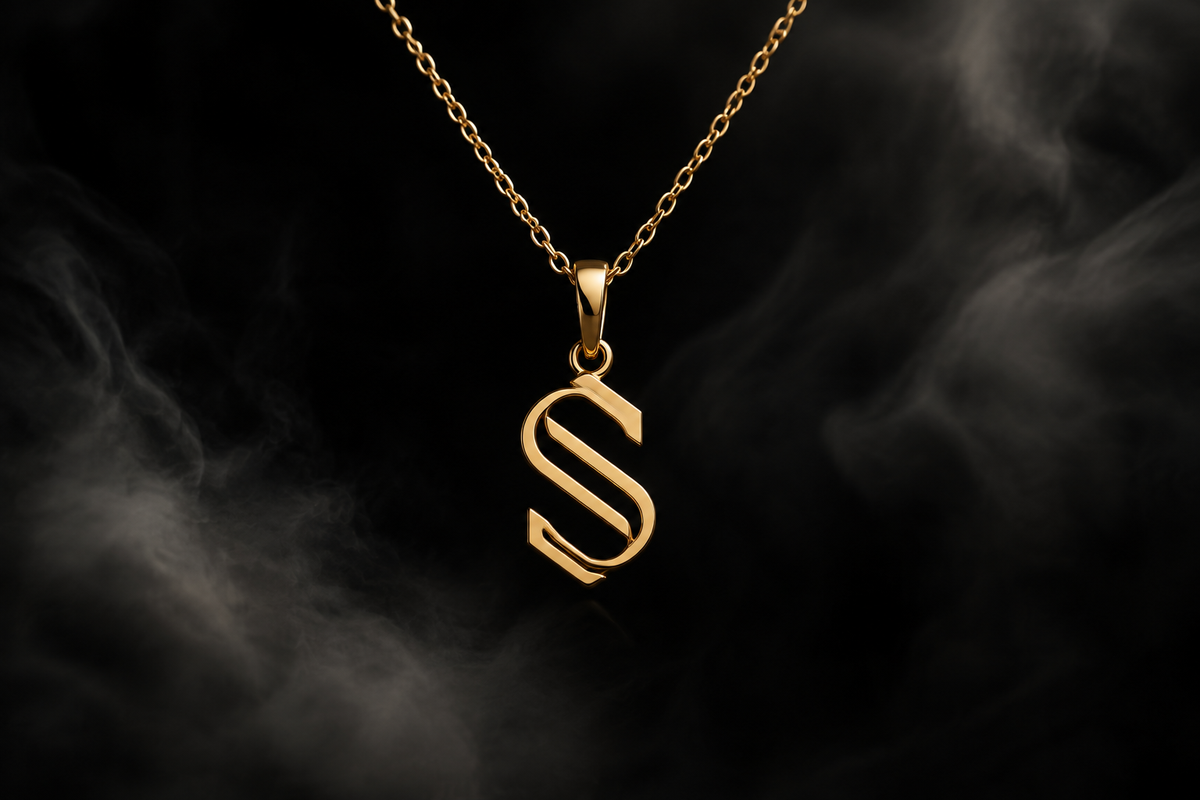 The Saintarini S Pendant — the house letterform in polished gold on a dark backdrop (placeholder image, to be replaced with the production photograph)